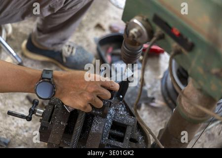 Focused male worker hand operating an industrial drill press in workshop. skilled mechanic showing intense concentration while using heavy machinery f Stock Photo