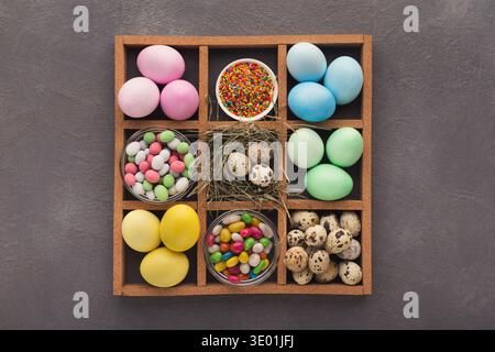 Colored easter eggs and small candies in frame on gray background Stock Photo