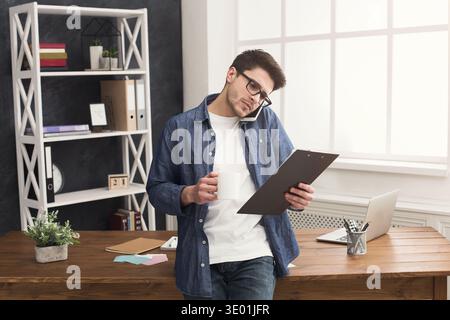 Pensive young businessman talking on mobile and reading documents Stock Photo