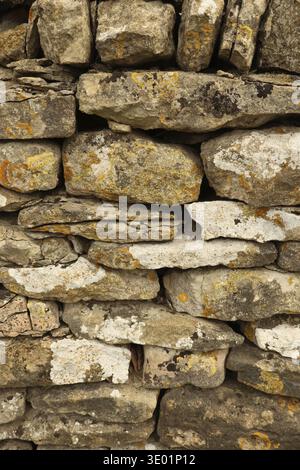 Dry stone wall texture showing stacked rocks with varied shapes, tones, and patches of yellow and white lichen. Cotswolds, England, United Kingdom Stock Photo