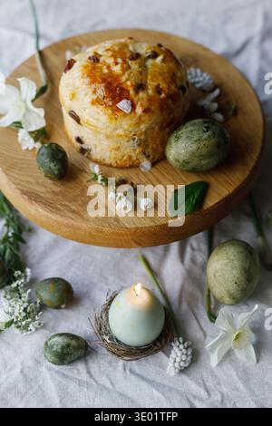 Easter celebration. Stylish green easter eggs, easter bread, candle and cherry blossoms on linen napkin, space for text. Atmospheric authentic Easter Stock Photo