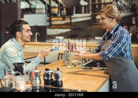Smiling barista taking payment from client Stock Photo