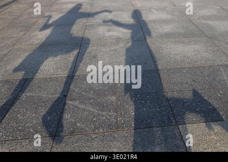 Two funny shadows of women facing each other on the square in the city. Walks of two girlfriends in the streets. Having fun, grimacing in the sun, mak Stock Photo