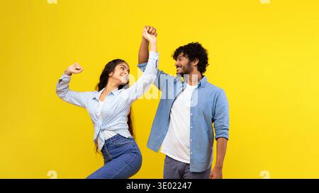 Couple Dancing Together in Front of a Bright Yellow Background During a Joyful Moment Stock Photo