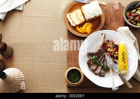 Overhead view of South American dinner with plate of steak, corn, kidney bean salad and salsa verde Stock Photo