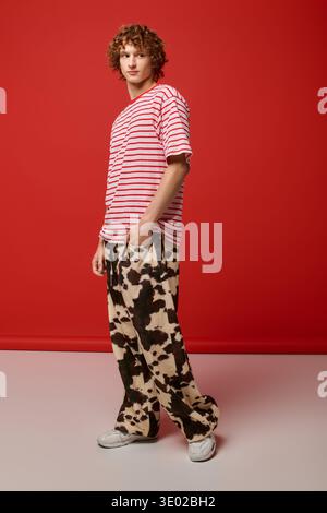 A fashionable young man with curly hair stands confidently in a red studio space Stock Photo
