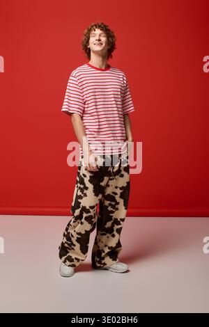 A fashionable young man with curly hair stands confidently in a red studio. Stock Photo