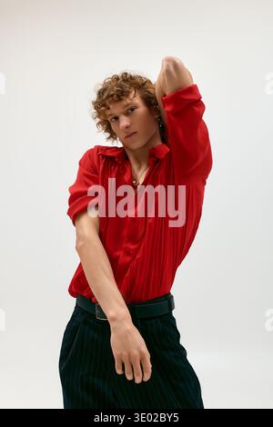 Curly-haired young man showcases fashion flair in a red shirt, striking a confident pose. Stock Photo
