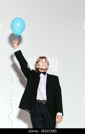 A young man with curly hair smiles brightly while holding a blue balloon in a festive studio. Stock Photo
