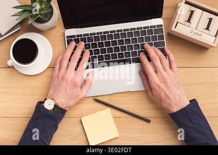 Man typing on laptop computer on wooden table. Stock Photo