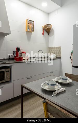 Contemporary kitchen featuring white cabinets, stainless steel sink, coffee maker, microwave, and set dining table Stock Photo