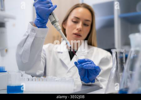 Laboratory technician using a micropipette to transfer colored liquid into microcentrifuge tubes at a clean research station. Stock Photo