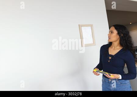 Adult woman measuring frame at home in navy top and jeans with yellow level, copy space. Decor, art, hanging, measurement, tool, interior, residence Stock Photo