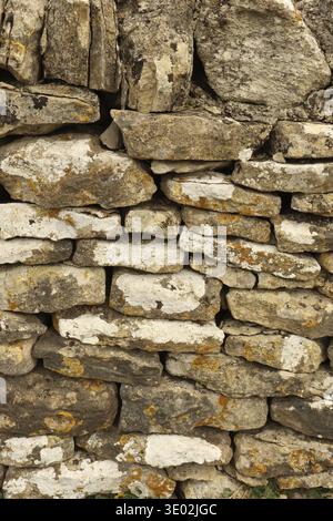 Dry stone wall built from various shaped, textured rocks creating an ancient, rustic background. Lichen, moss, and weathering present on surface. Cots Stock Photo