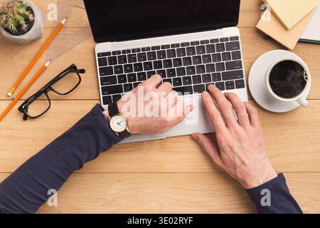 Man typing on laptop computer on wooden table. Stock Photo
