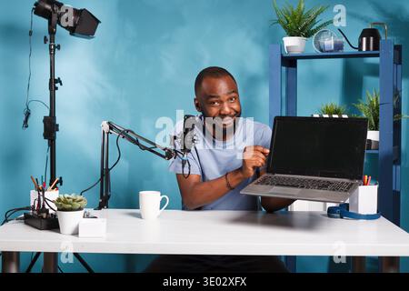 Vlogger presenting laptop and testing features while creating web content for internet channel. Smiling blogger showing portable computer giveaway gift while recording video Stock Photo