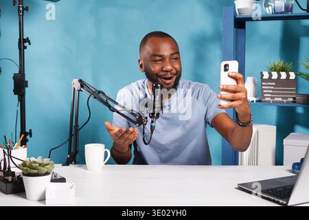 Blogger creating engaging content with smartphone and speaking to subscribers. Smiling african american vlogger talking while live streaming on social media network with mobile phone Stock Photo