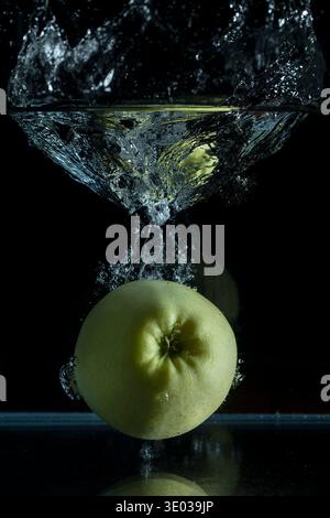 A green apple falls into a glass container, raising a large splash Stock Photo
