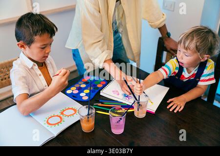 Asian family at home - family spending quality time together, children expressing creativity with watercolors, mom supporting kids learning and develo Stock Photo