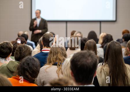 Audience listening to speaker at conference, people attending presentation in meeting room with projection screen. Stock Photo