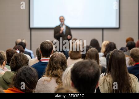 Conference audience listening to speaker during presentation in lecture hall, professional seminar atmosphere, focus, learning, engagement. Stock Photo