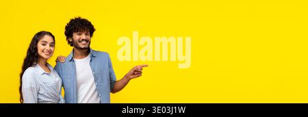 Two People Smiling and Pointing at Something on a Bright Yellow Background Stock Photo