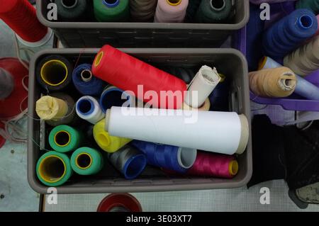 Vibrant Spools And Tools Arranged, Colorful Thread Rolls Nested In Plastic Box, White Paper Tube Resting Among Coils, Compact Creative Setup For Sewin Stock Photo