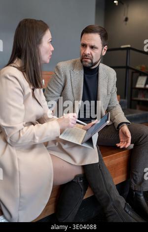 Man and woman sitting side by side, using stylus with digital tablet in bright office. Stylus, digital tablet, bright, teamwork, side by side. Stock Photo