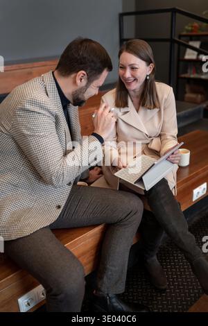 Two colleagues collaborating and writing on a piece of paper while sitting indoors on wooden seating. Collaboration, writing, indoor, teamwork Stock Photo
