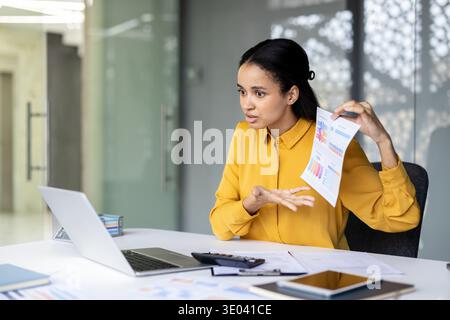Successful businesswoman presenting financial charts during a video conference, discussing project results and data analysis with colleagues remotely on a laptop in a modern office workplace Stock Photo