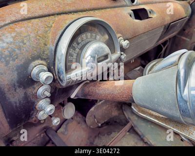 The steering column extends from underneath the odometer and dashboard on an old, rusting car in a junkyard. Stock Photo