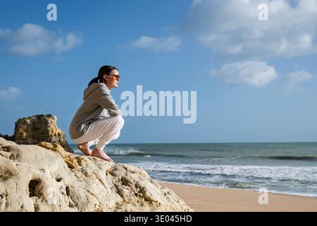 sporty woman sitting on rocks by the sea looking at the view Stock Photo