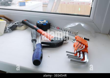 Homeowner Preparing For Fixing Window. Bright Window Sill With Essential Repair Tools Displayed. Various Repair Implements Arranged On Sunlightlit Stock Photo