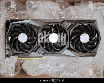 Brand new triple fan graphics card resting in bubble wrap inside an open shipping box, top view of modern high end GPU hardware protected for delivery Stock Photo