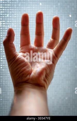 Human hand reaching toward light through textured glass with prism reflections. Stock Photo