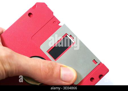 Hand showcasing a red floppy disk magnetic surface, closeup of vintage data storage media and retro technology, old school file backup concept, obsole Stock Photo