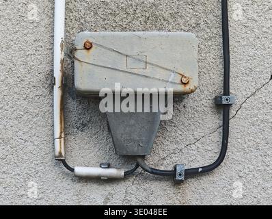 Old wall mounted electrical junction box with rusted screws and conduit on cracked stucco facade, frontal closeup of aging broken vintage exterior pow Stock Photo