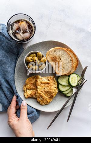 A hearty keto breakfast featuring scrambled eggs, fresh cucumber slices, flavorful Greek olives, and toasted bread served with iced coffee on a gray p Stock Photo