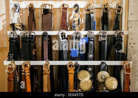 A diverse collection of stylish leather and metal belts neatly displayed on a clothing store rack. Each belt showcases various buckle designs and colo Stock Photo