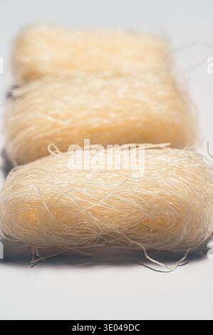 Close-up of uncooked rice noodles neatly arranged in bundles on a white surface. The translucent noodles create an intricate texture, showcasing their Stock Photo