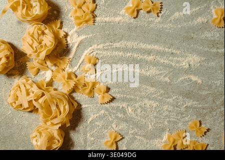 Different types of Italian pasta including farfalle and tagliatelle are scattered on a floured surface. The image captures a rustic, culinary atmosphe Stock Photo