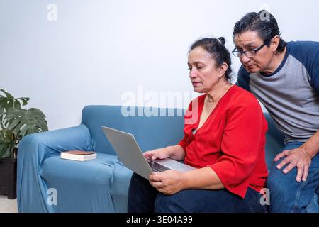Senior couple working together on a laptop, learning and communicating online while sitting on a sofa Stock Photo