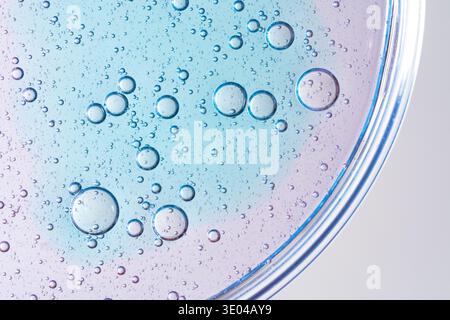 Macro photograph of air bubbles in a liquid-filled petri dish, creating an abstract texture. The bubbles appear in various sizes against a pastel blue Stock Photo