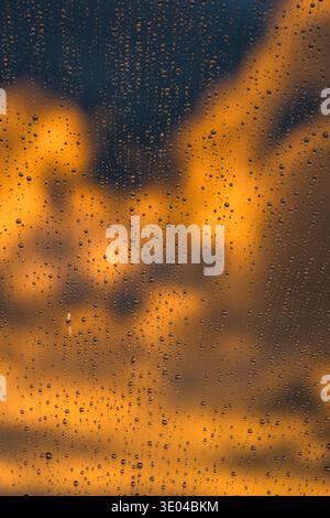 Abstract image of raindrops on glass at sunset. The blurred skyline in the background creates a stunning contrast of warm and cool tones, evoking a se Stock Photo