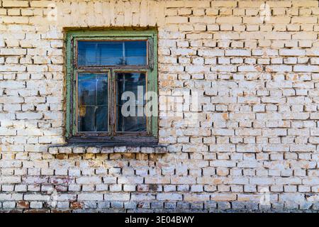 Old Window on Weathered Brick Wall. A rustic old window set in a worn brick wall, showing aged texture, peeling paint, and vintage architectural Stock Photo