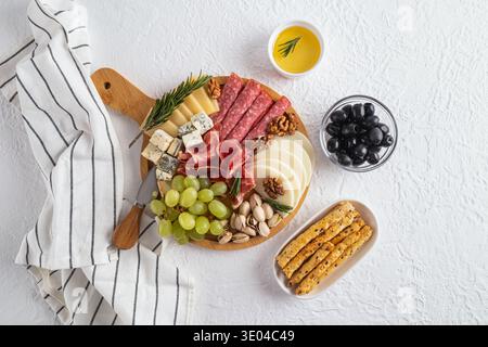 A beautifully arranged cheese platter featuring a variety of sliced cheeses, assorted meats, fresh grapes, nuts, and crispy breadsticks, ideal for gou Stock Photo