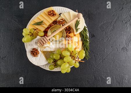 An elegant cheese platter featuring assorted cheeses, fresh green grapes, crunchy walnuts, and a honey dip, perfect for a gourmet presentation on a da Stock Photo