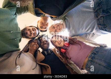 diverse group of young students standing in circle looking down and smiling together outdoors symbolizing friendship youth community and connection Stock Photo