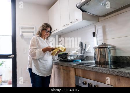 Senior woman responsibly cleaning dishes in her home kitchen Stock Photo