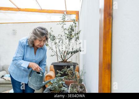 Senior woman is nurturing plants in pots with a watering can, enjoying her gardening hobby Stock Photo